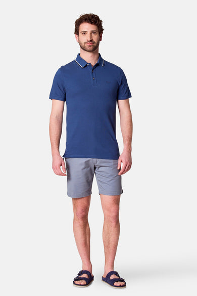 Man in blauw poloshirt en grijze shorts, staand.