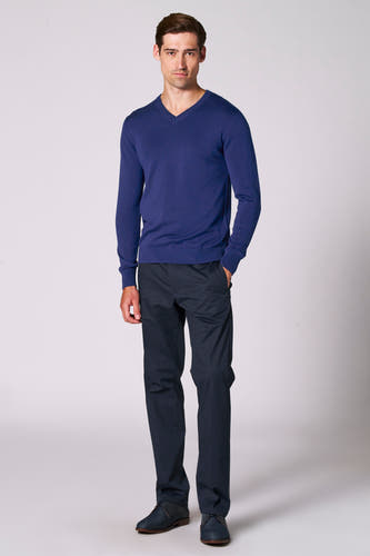 Pull à col V bleu de Bruce & Butler, associé à un pantalon et des des desers sombres.