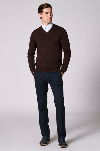 Pull à col V brun de Bruce & Butler, porté avec un chemisier bleu clair et un pantalon bleu marine avec des baskets.