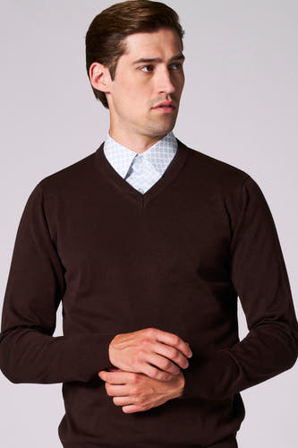 Pull à col V brun de Bruce & Butler, porté sur une chemise bleue claire imprimée, mains croisées.