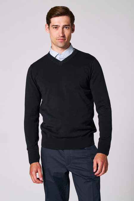 Pull à col V bleu marine de Bruce & Butler, porté sur un chemisier bleu clair imprimé et un pantalon foncé.