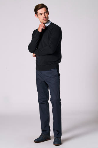 Pull à col V bleu marine de Bruce & Butler, porté sur une chemise à fines rayures, associé à un pantalon et des chaussures foncés.
