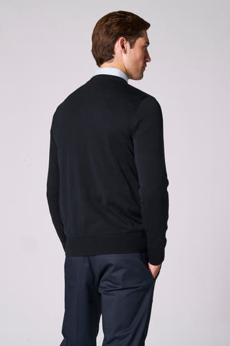 Pull à col V bleu marine de Bruce & Butler, avec un motif subtilement structuré, combiné avec une chemise et un pantalon.