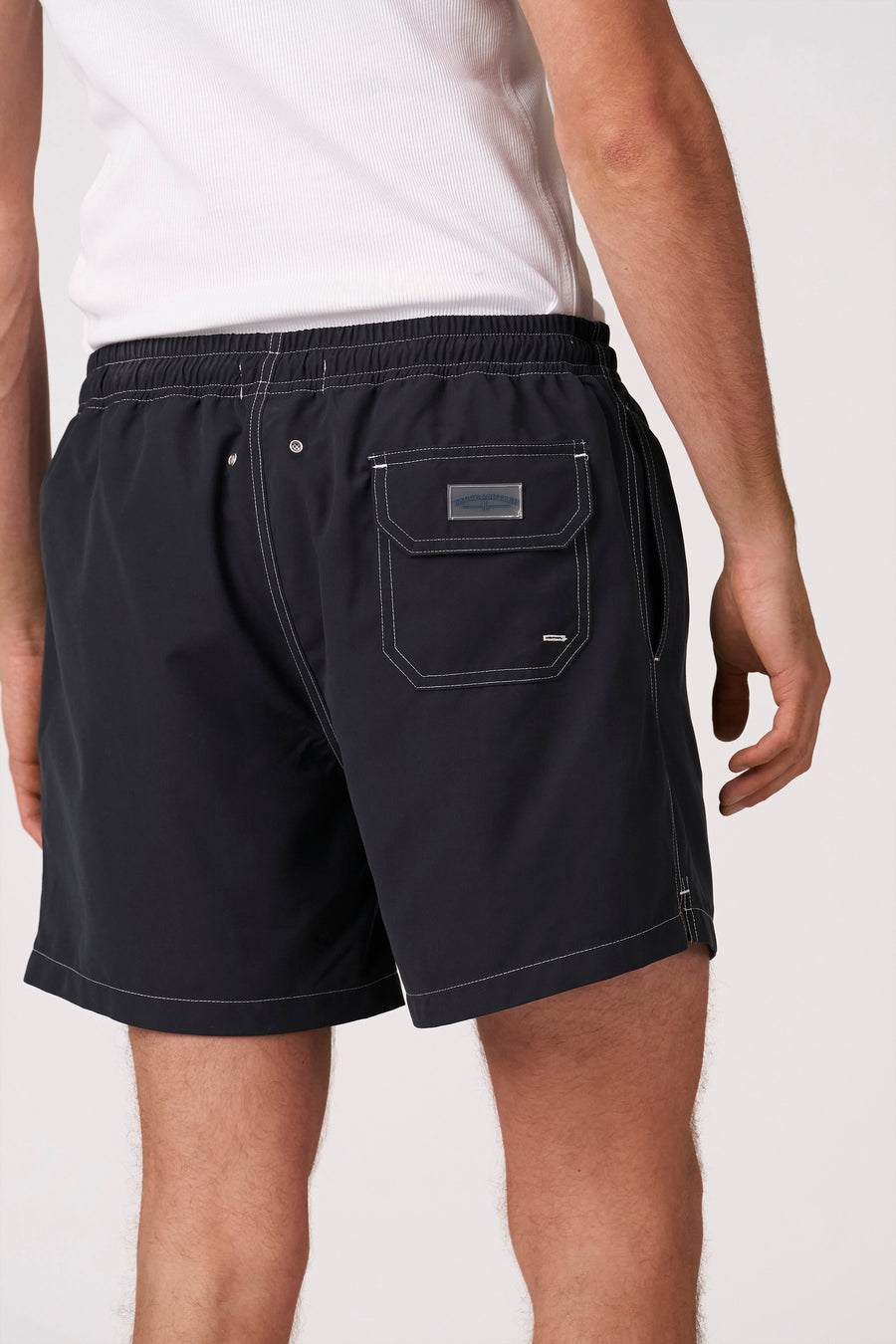 Short de bain noir de Bruce & Butler avec surpiqûres contrastées blanches, taille élastique et poche arrière avec étiquette, photographié de dos.