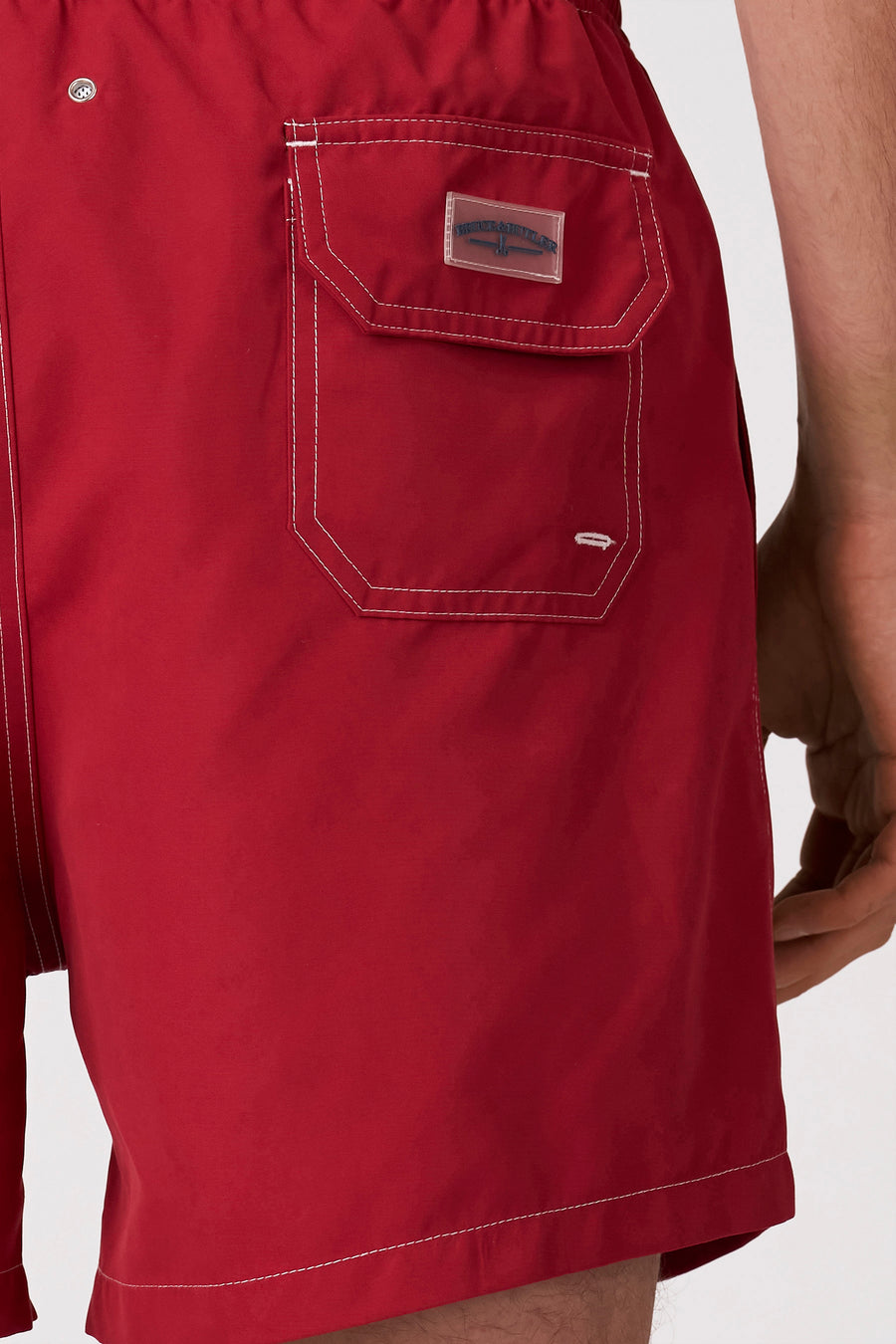 Short de bain rouge de Bruce & Butler avec surpiqûres contrastées blanches, une poche arrière avec écusson logo transparent et un œillet argenté.
