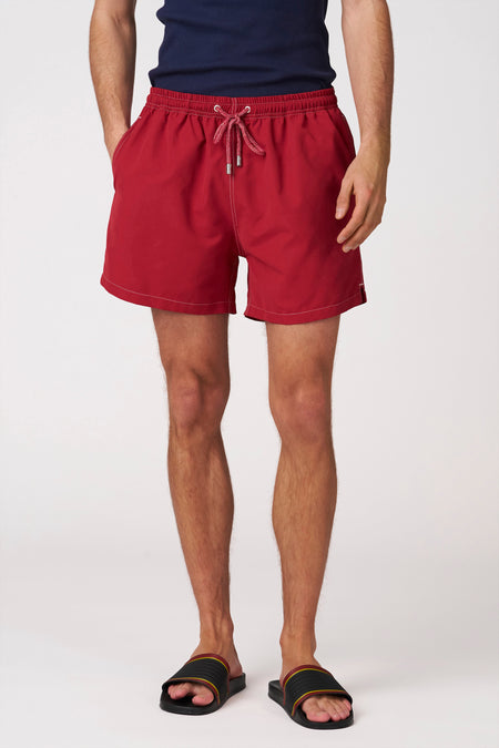 Short de bain rouge de Bruce & Butler avec cordon de serrage rouge, coutures blanches et poches latérales, porté par un homme.