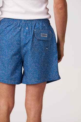 Short de bain bleu de Bruce & Butler avec motif de feuilles fines, taille élastique avec surpiqûres blanches et œillets métalliques, et poche à rabat à l'arrière, vue de dos.