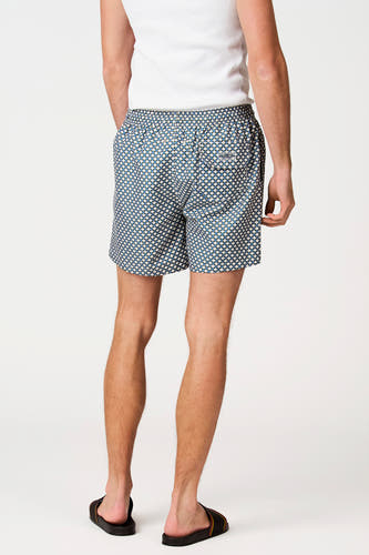Short de bain multicolore de Bruce & Butler avec motif géométrique et poche arrière, vue de dos, porté avec une chemise blanche et des sandales.