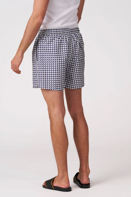 Blauw-witte pied-de-poule zwemshort van Bruce & Butler, gedragen door een man van achteren met een witte tanktop en zwarte sandalen.