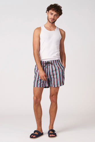 Short de bain multicolore de Bruce & Butler avec des rayures verticales marron, vert, rose, bleu clair et blanc, et un cordon de serrage marron foncé, porté avec un débardeur blanc et des sandales.