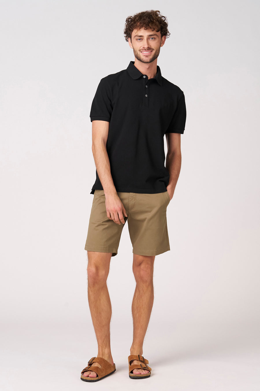 Polo noire à manches courtes de Bruce & Butler, portée avec un short kaki et des sandales marron.
