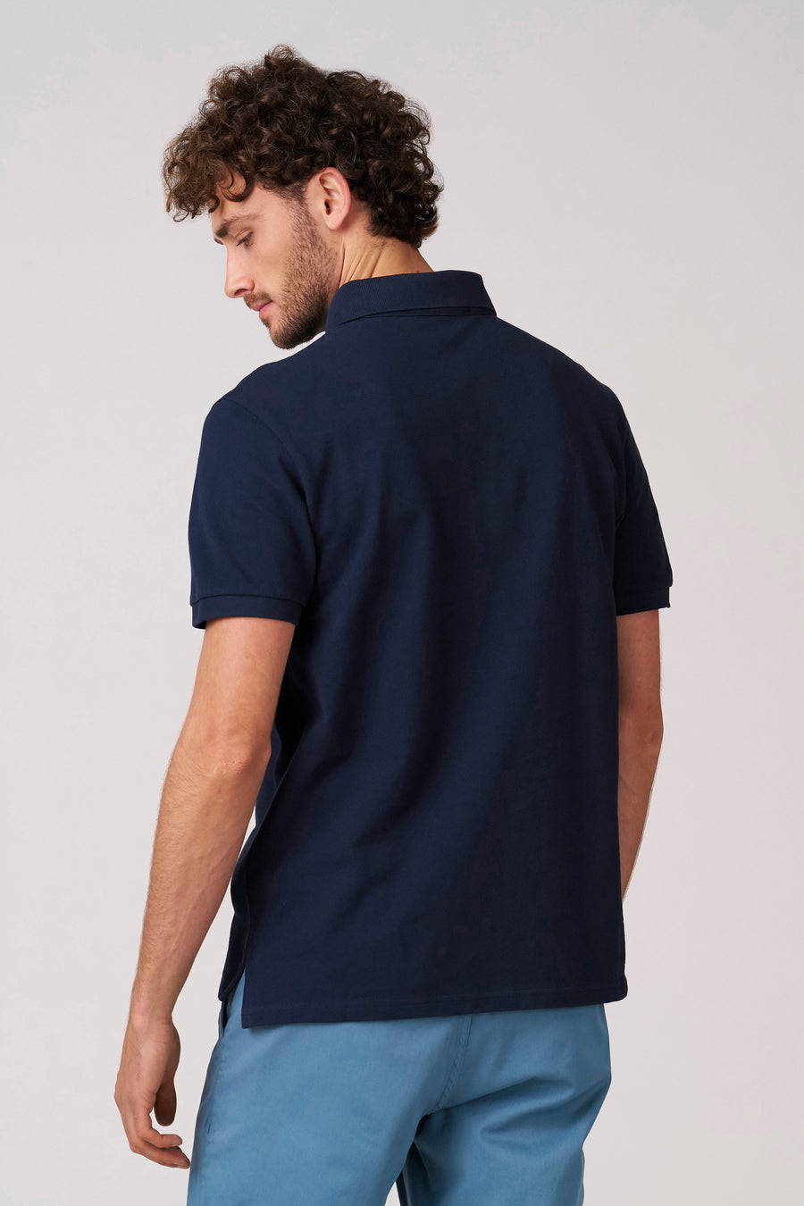 Blauwe polo met korte mouwen van Bruce & Butler, gezien van achteren, gedragen met een lichtblauwe broek.
