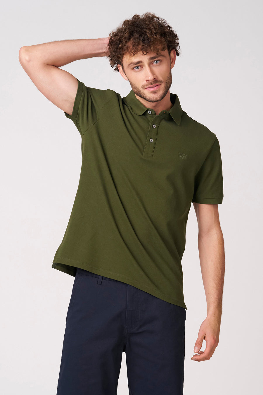 Polo verte à manches courtes verte de Bruce & Butler, vue de dos avec les bras croisés et un pantalon foncé.