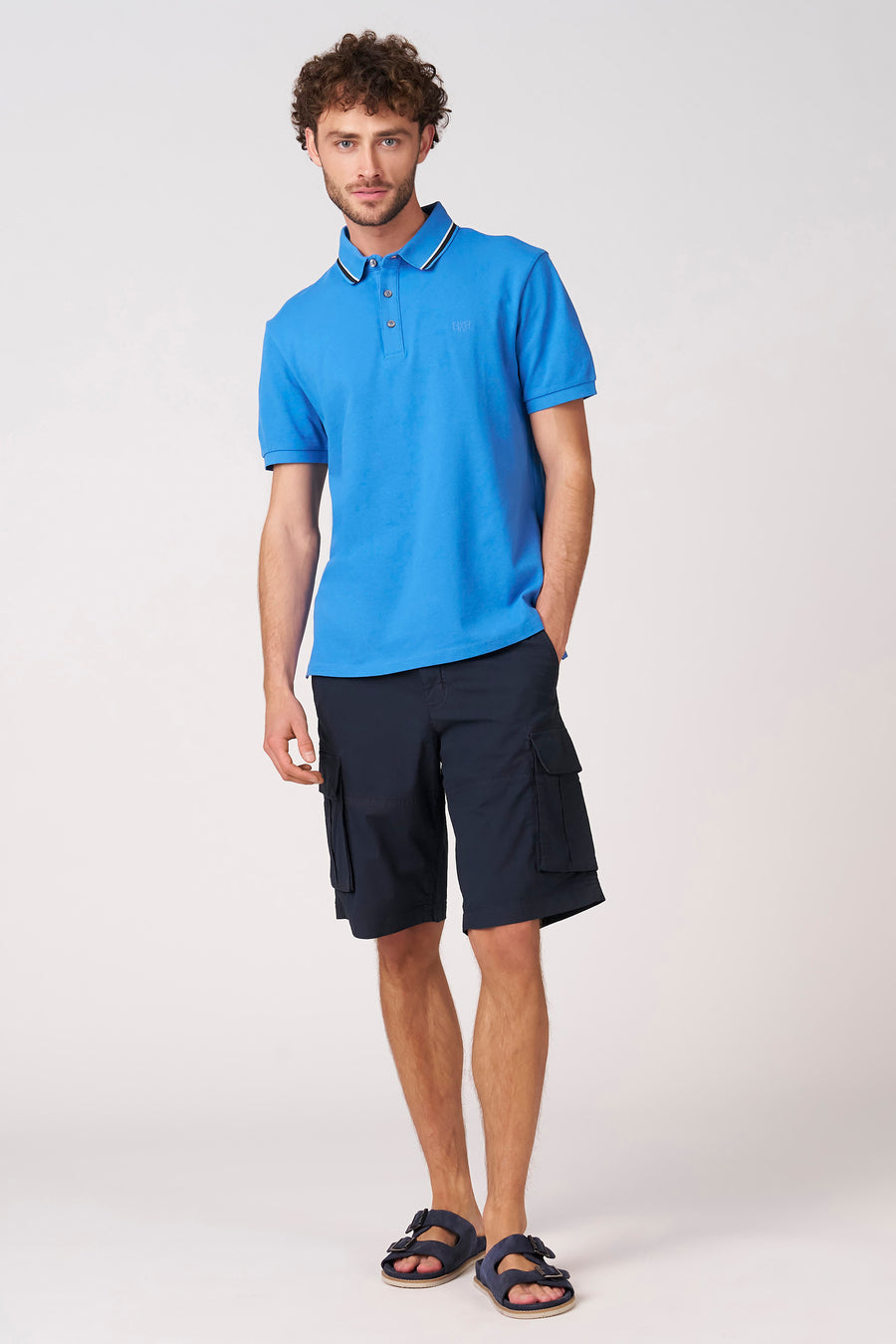 Polo bleu à manches courtes de Bruce & Butler, avec une rayure blanche sur le col et un short cargo.