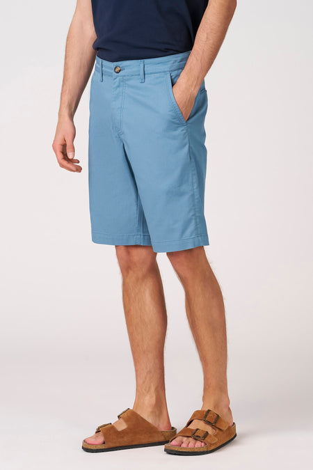 Blauwe short van Bruce & Butler, met steekzak en gedragen met bruine sandalen.
