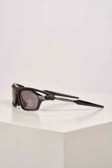 Lunettes de soleil noires de Cyclo Club Marcel, posées sur une surface blanche, vue de face.