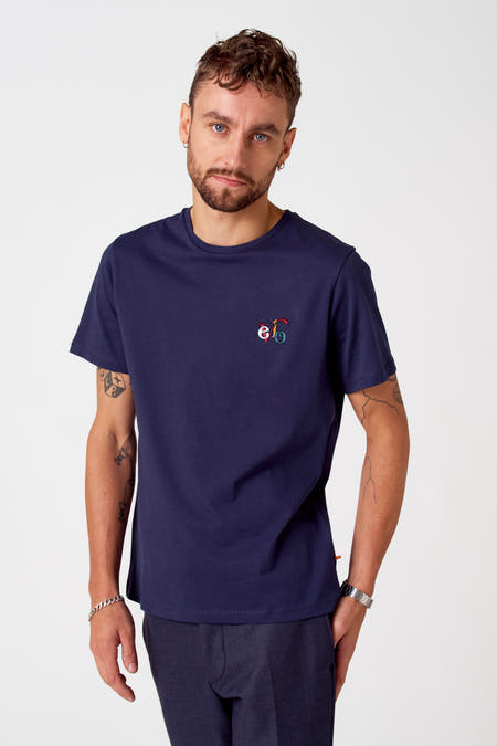 T-shirt bleu à manches courtes de Cyclo Club Marcel, vue arrière, porté avec un pantalon foncé et une montre argentée, avec des tatouages sur les bras.