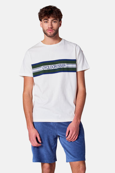 T-shirt blanc à manches courtes de Cyclo Club Marcel, avec logo sur la manche, associé à des short en corduroy bleu.