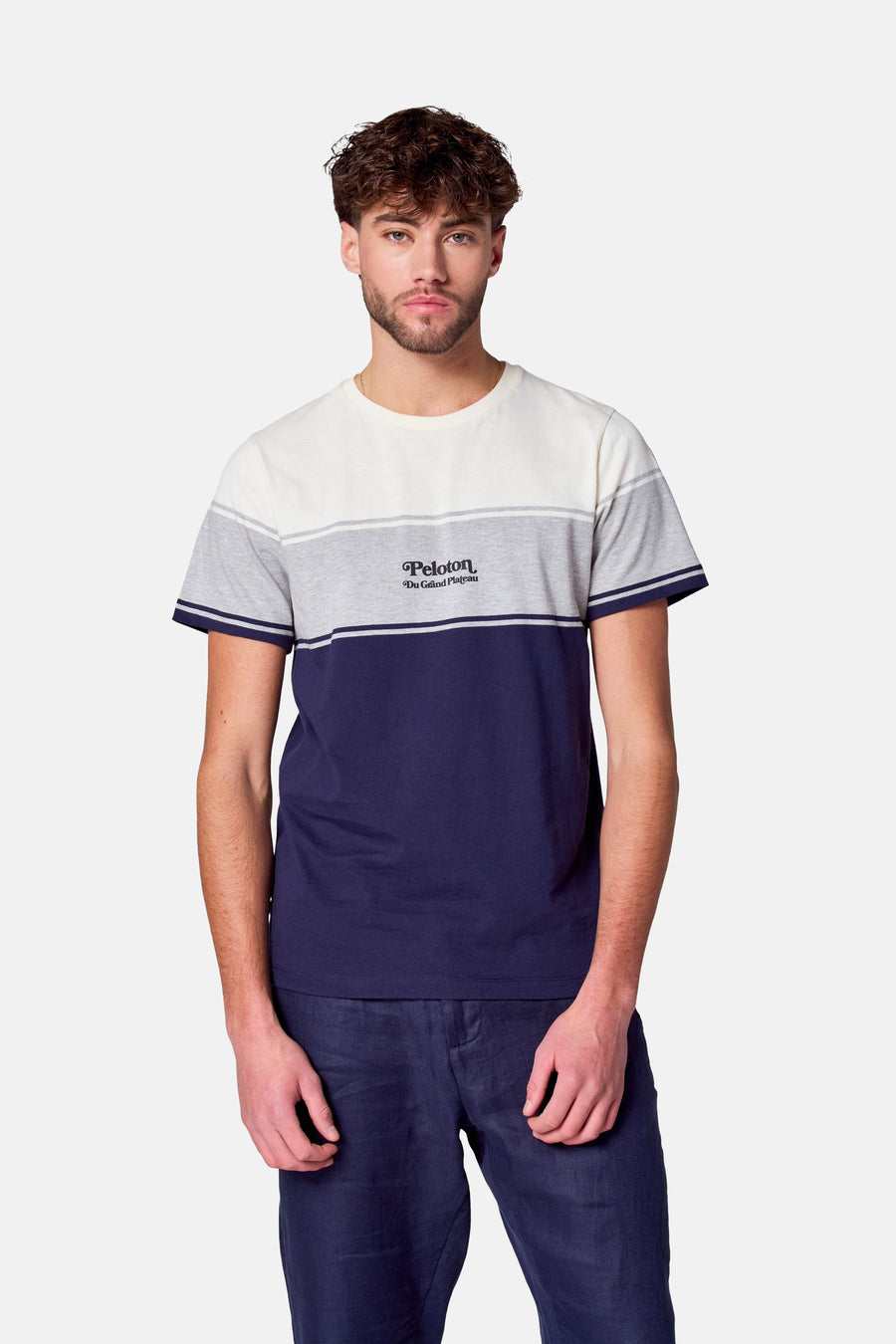 Man met gestreept t-shirt en blauwe broek op witte achtergrond.