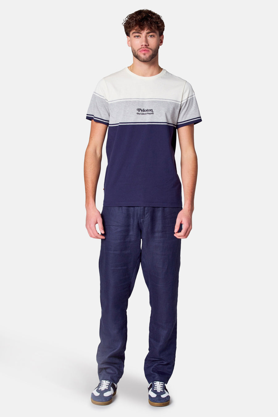 Man staat, blauwe broek, gestreept shirt, sneakers.
