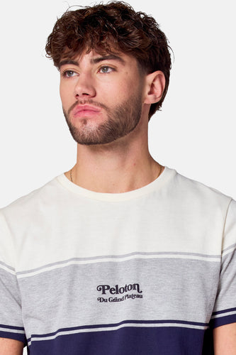 Een man met krullend haar in een gestreept wit, grijs en blauw t-shirt.