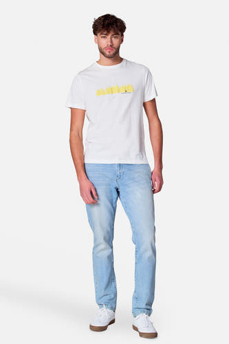 Homme debout, t-shirt blanc avec imprimé jaune, jeans bleu clair, baskets blanches.