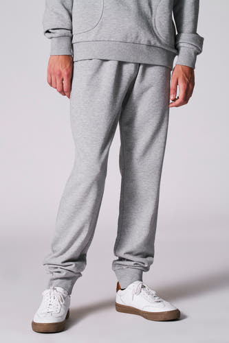 Grijze jogging van Cyclo Club Marcel, met elastische boorden en witte sneakers met bruine zolen.
