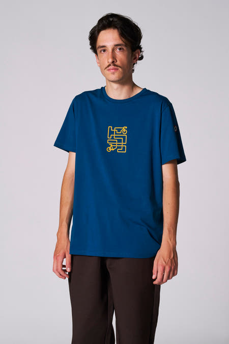 T-shirt bleu à manches courtes du Cyclo Club Marcel, avec un graphique de vélo jaune sur la poitrine, associé à un pantalon marron.