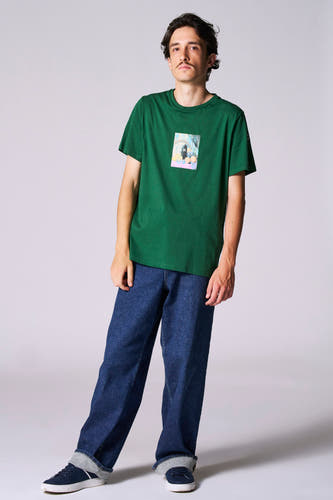 T-shirt vert avec manches courtes de Cyclo Club Marcel, avec une petite image sur la poitrine, associé à des jeans bleus foncés et des baskets.