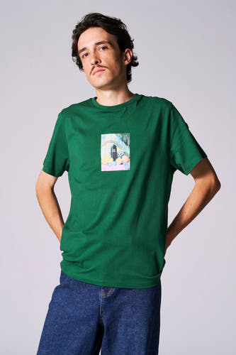 T-shirt vert avec manches courtes de Cyclo Club Marcel, imprimé sur la poitrine, porté avec un jean bleu marine.