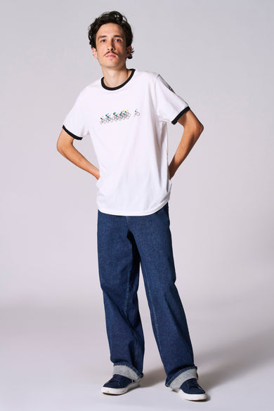 T-shirt blanc à manches courtes de Cyclo Club Marcel, avec une impression de cyclistes et porté avec des jeans et des baskets.