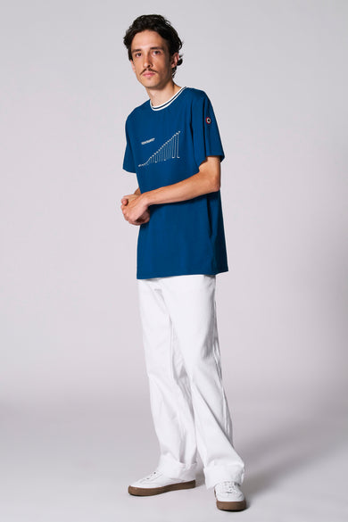 T-shirt bleu à manches courtes du Cyclo Club Marcel, avec une impression graphique blanche et un short et des chaussures blancs.