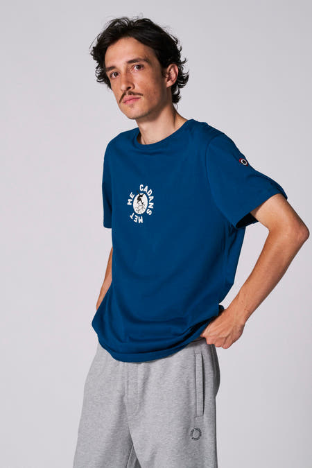 T-shirt bleu à manches courtes du Cyclo Club Marcel, avec une impression blanche et porté avec un short de jogging gris.