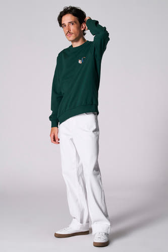 T-shirt vert de Cyclo Club Marcel, porté avec un pantalon blanc et des baskets à semelles brunes.