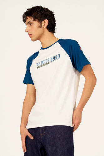 T-shirt blanc à manches courtes de Cyclo Club Marcel, avec manches raglan bleues et jean foncé.