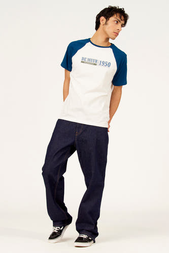 T-shirt blanc à manches courtes Cyclo Club Marcel, avec manches raglan bleues, porté avec un jean bleu foncé et des baskets noires.