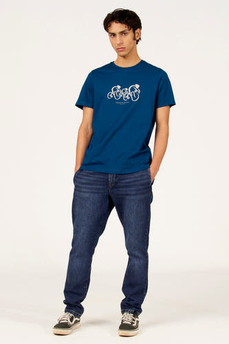 T-shirt bleu à manches courtes de Cyclo Club Marcel, avec imprimé blanc, combiné avec un jean foncé et des baskets.