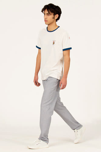 T-shirt blanc à manches courtes Cyclo Club Marcel, avec bordures bleues et logo sur la poitrine, porté avec un pantalon gris et des baskets blanches.