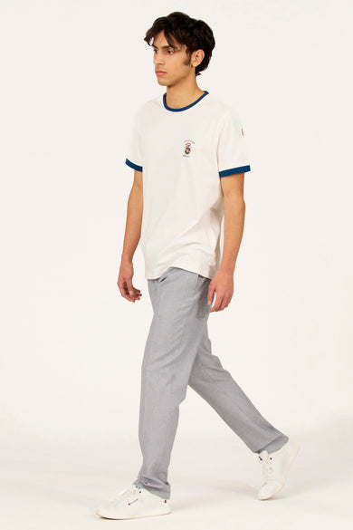T-shirt blanc à manches courtes Cyclo Club Marcel, avec bordures bleues et logo sur la poitrine, porté avec un pantalon gris et des baskets blanches.