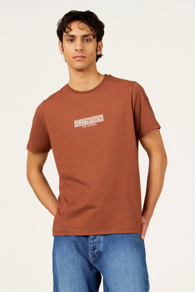 T-shirt marron à manches courtes Cyclo Club Marcel, avec logo sur la manche et associé à un jean.