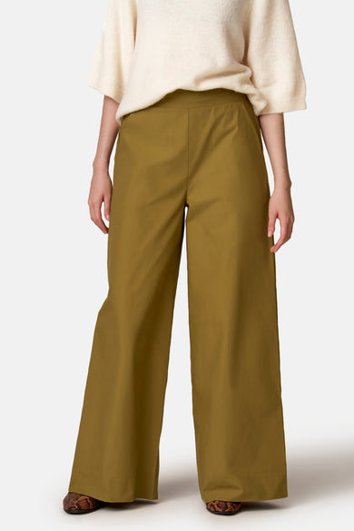 Pantalon vert COPINES D'ANVERS à jambes larges et poches italiennes, porté avec un pull de couleur crème et des mocassins marron à imprimé serpent.