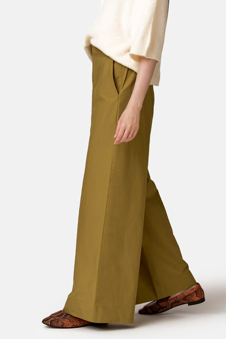 Groene broek van COPINES D'ANVERS met wijde pijpen en steekzakken, gedragen met een crèmekleurige trui en bruine loafers met slangenprint.