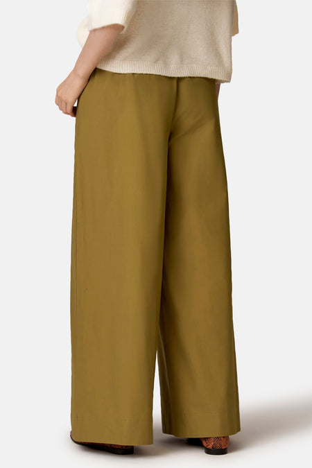 Pantalon vert de COPINES D'ANVERS à jambes larges, vu de dos, porté avec un pull beige et des chaussures en cuir de serpent marron.