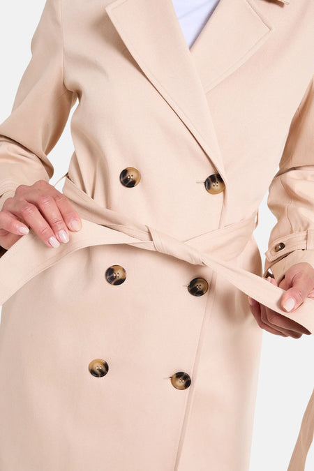 Manteau long beige de NAF NAF, boutonné avec une ceinture, double rangée de boutons.