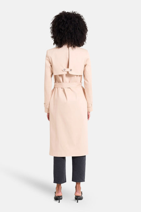 Manteau long beige de NAF NAF, vu de l'arrière, combiné avec des jeans foncés et des talons noirs.