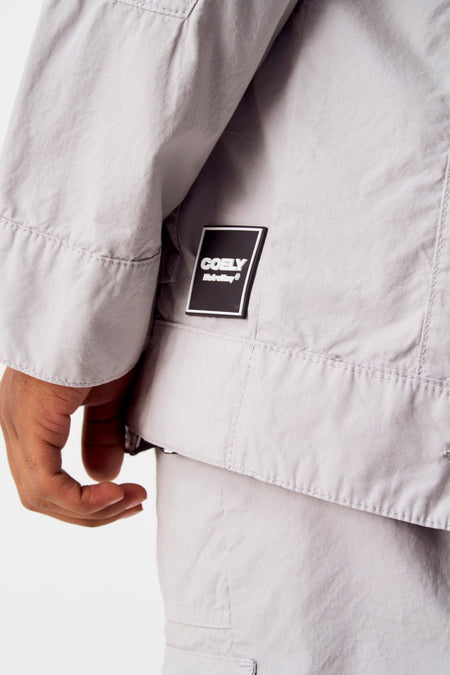 Veste grise de COELY, avec un logo carré sur la poitrine et des détails de boutons.