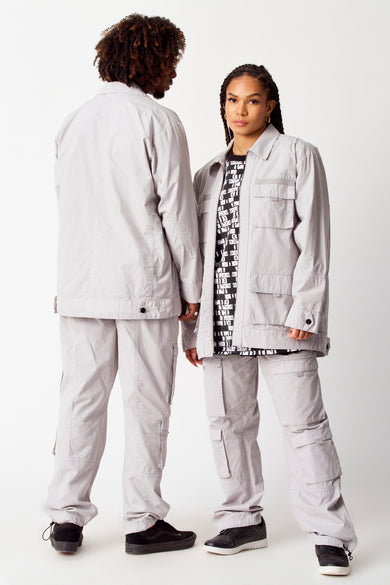 Manteau court gris de COELY, avec des poches broées et porté avec un pantalon à poches cargo.