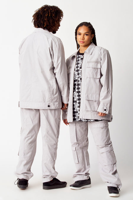 Manteau court gris de COELY, avec des poches broées et porté avec un pantalon à poches cargo.
