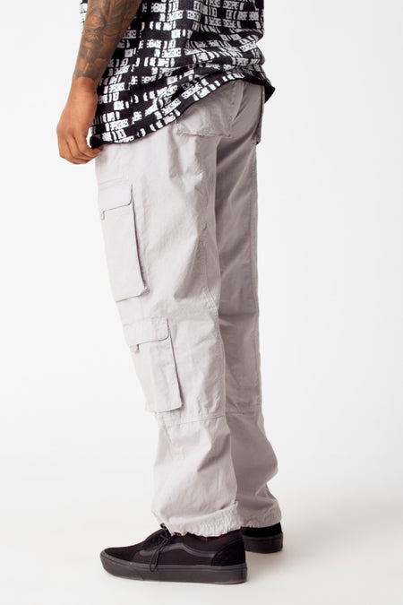 Jean cargo gris de Coely, avec poches et détails, associé à un t-shirt noir et blanc et des chaussures noires.