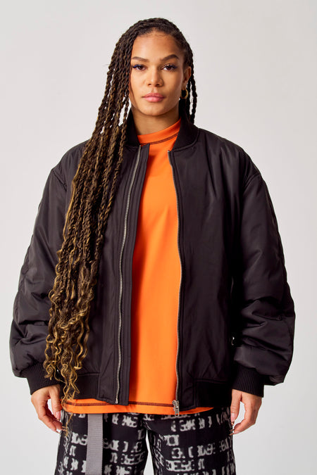 Manteau court noir de COELY, avec des longs cheveux et un t-shirt orange.